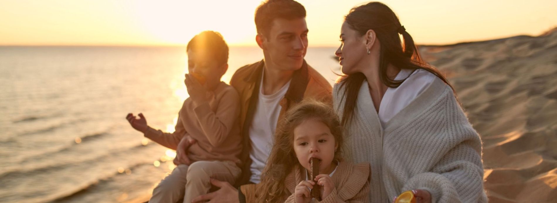 family sitting on the beach during sunset